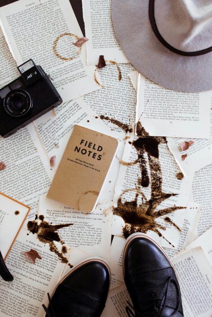 Creative flatlay featuring vintage camera, leather shoes, hat, and coffee-stained notes.